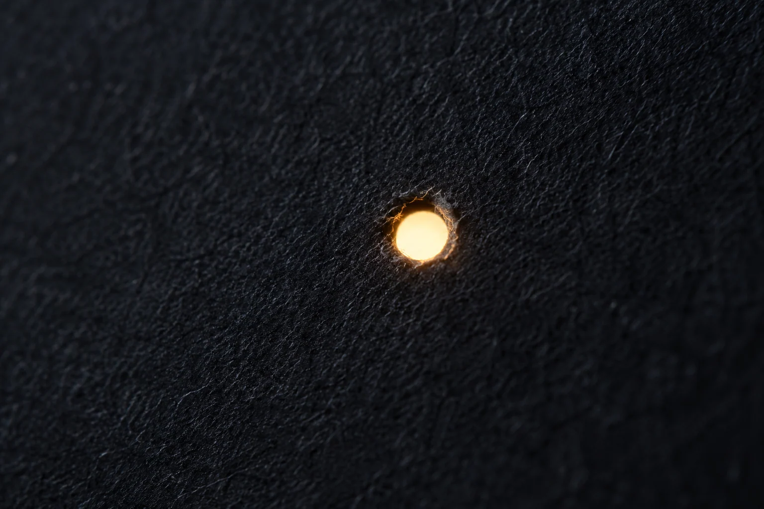 One warm point shines through the visible fibers of black paper.
